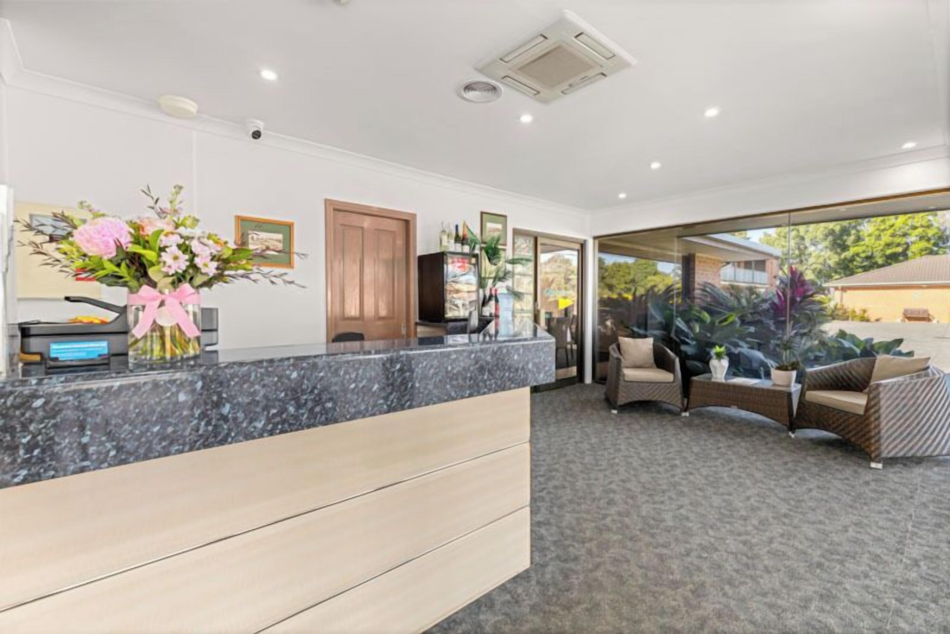 A reception area with a marble counter, wooden drawers, a large vase of flowers, and a view of the outdoors through glass doors.