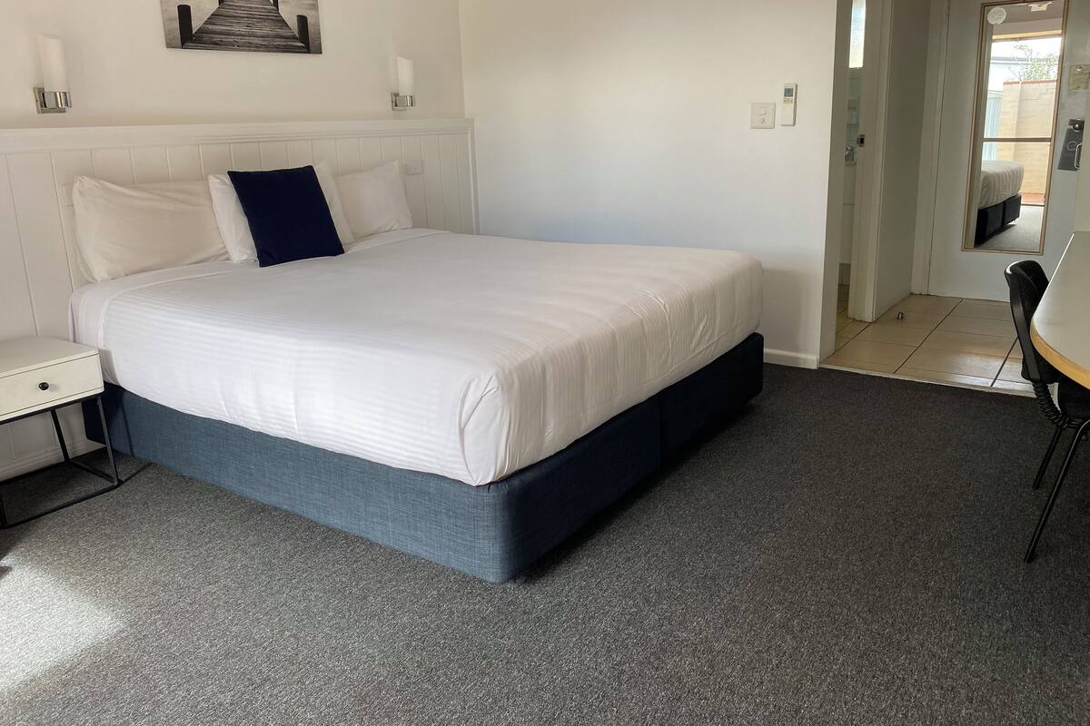 Quarto com cama, mesa de cabeceira e um quadro na parede.