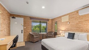 A hotel room with a brick wall, a bed, a desk, two chairs, a window with blinds, and a small balcony. - Macquarie Barracks Motor Inn (Port Macquarie)