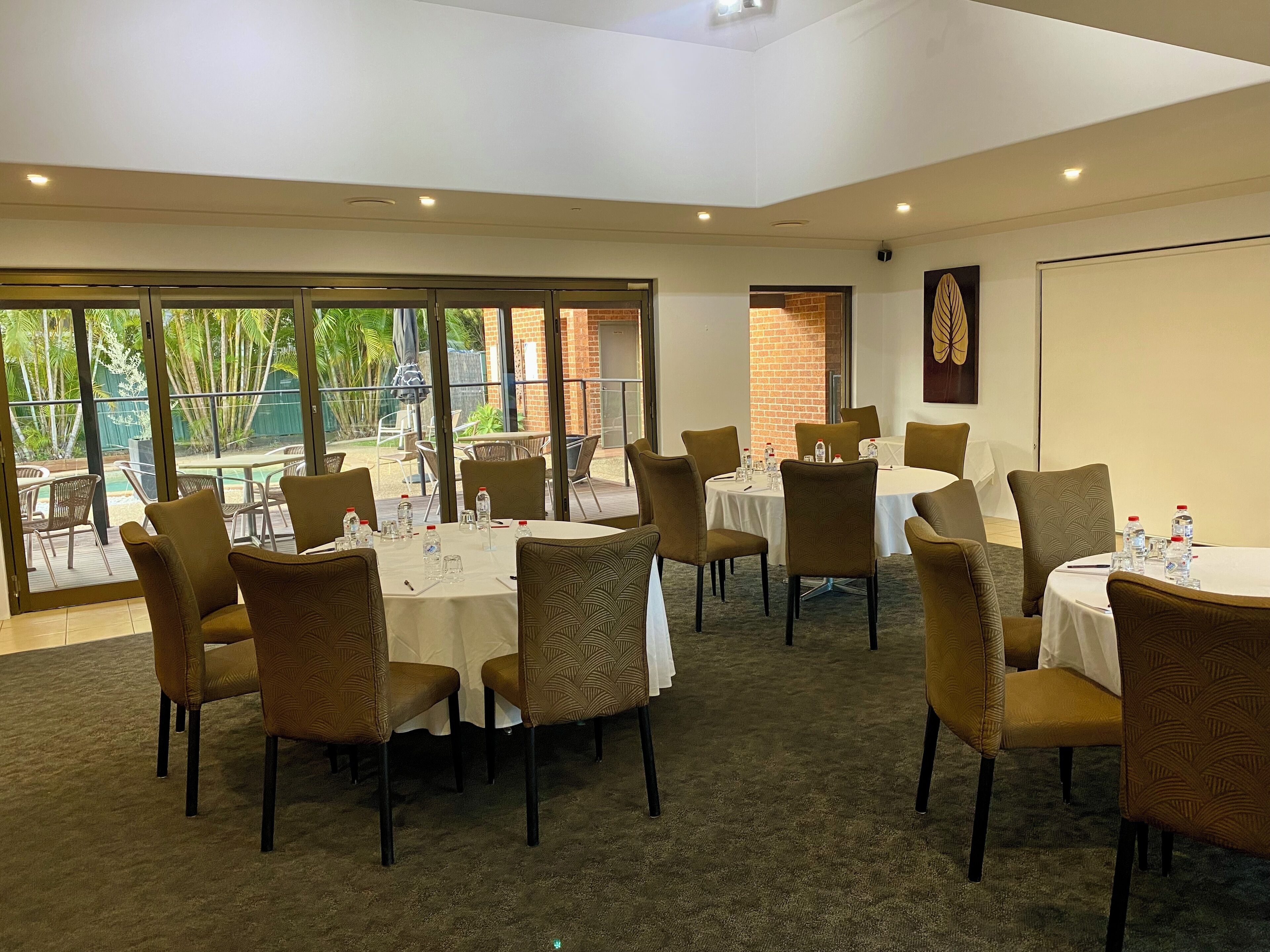 A conference room with round tables, chairs, and a large window overlooking a garden.