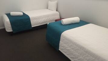 Two single beds with teal and white bedding, a red chair, and a window with blinds.