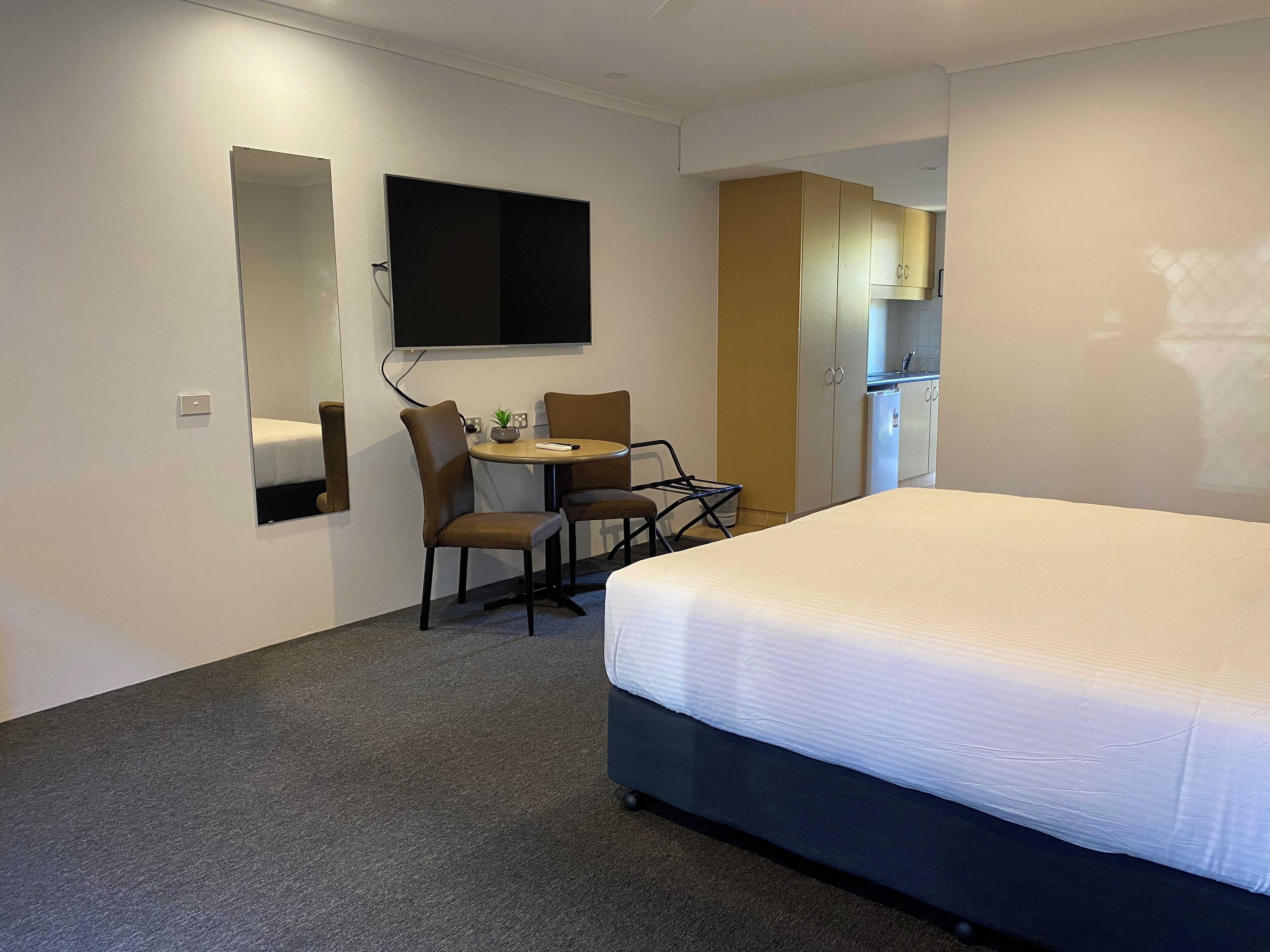 Une chambre d’hôtel comprenant un lit, un bureau avec une chaise, une petite table avec une plante, un téléviseur fixé au mur et un coin cuisine.