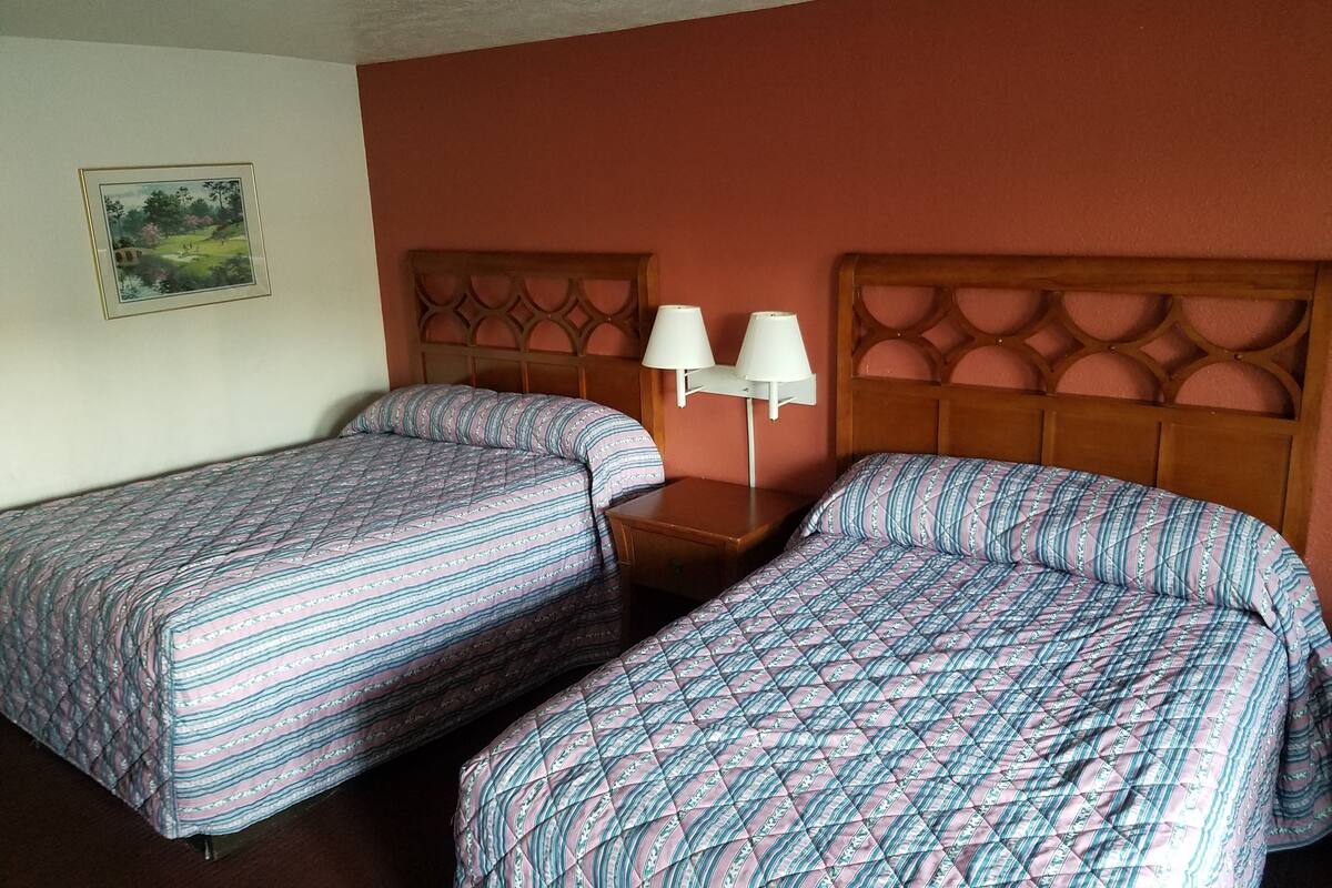 Une chambre d’hôtel avec deux lits simples, une table de chevet et une lampe fixée au mur.