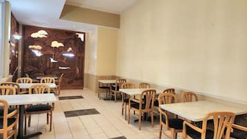 Un restaurante con mesas y sillas de madera, suelo de baldosas y una pared decorativa con un árbol y pájaros.