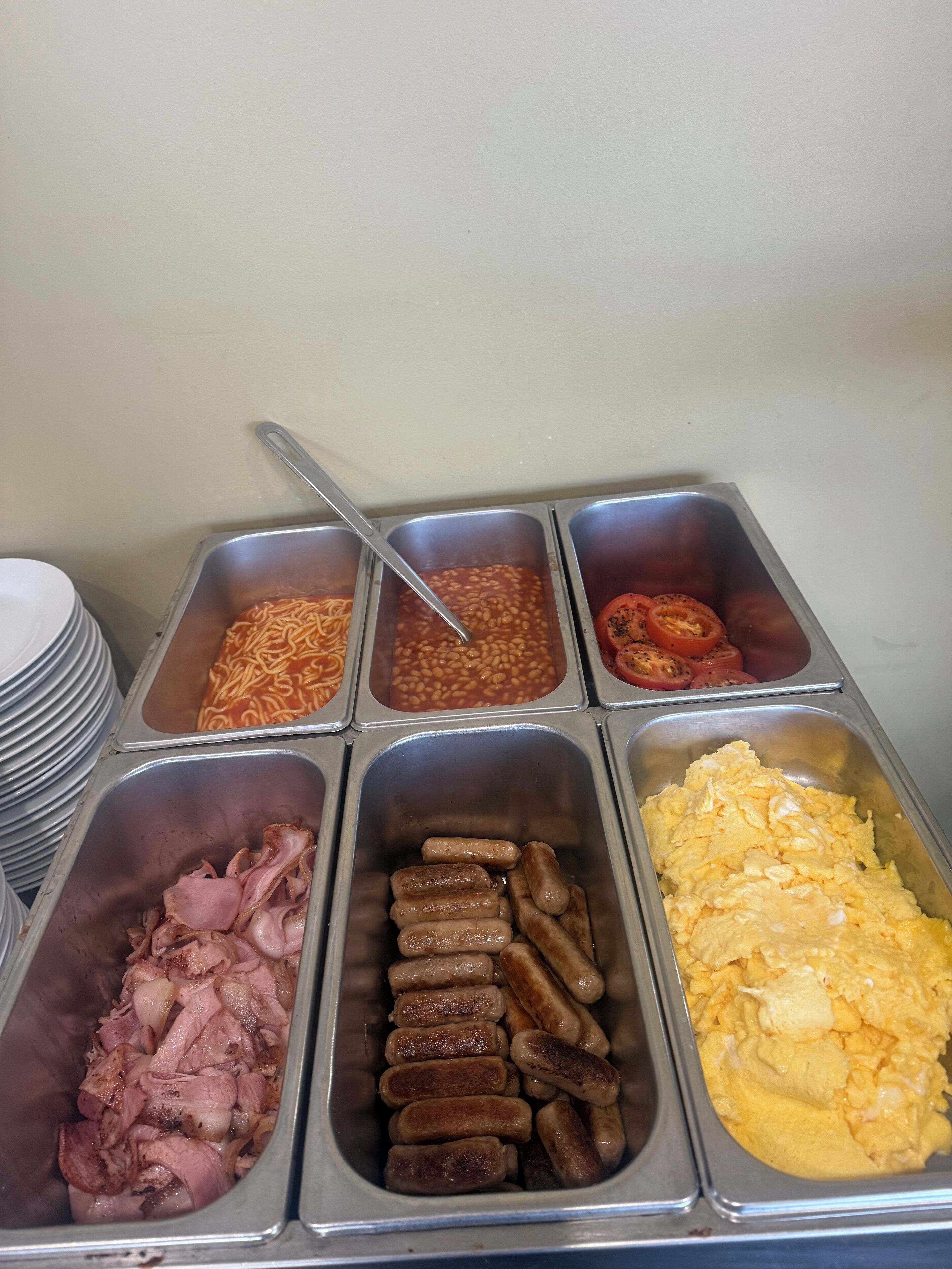 A buffet with various food options including sausages, eggs, beans, and tomatoes.