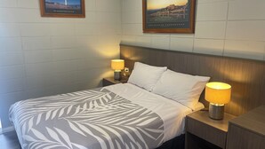 A hotel room with a bed, two bedside lamps, a framed picture on the wall, and a nightstand. - Cootamundra Gardens Motel (Cootamundra)