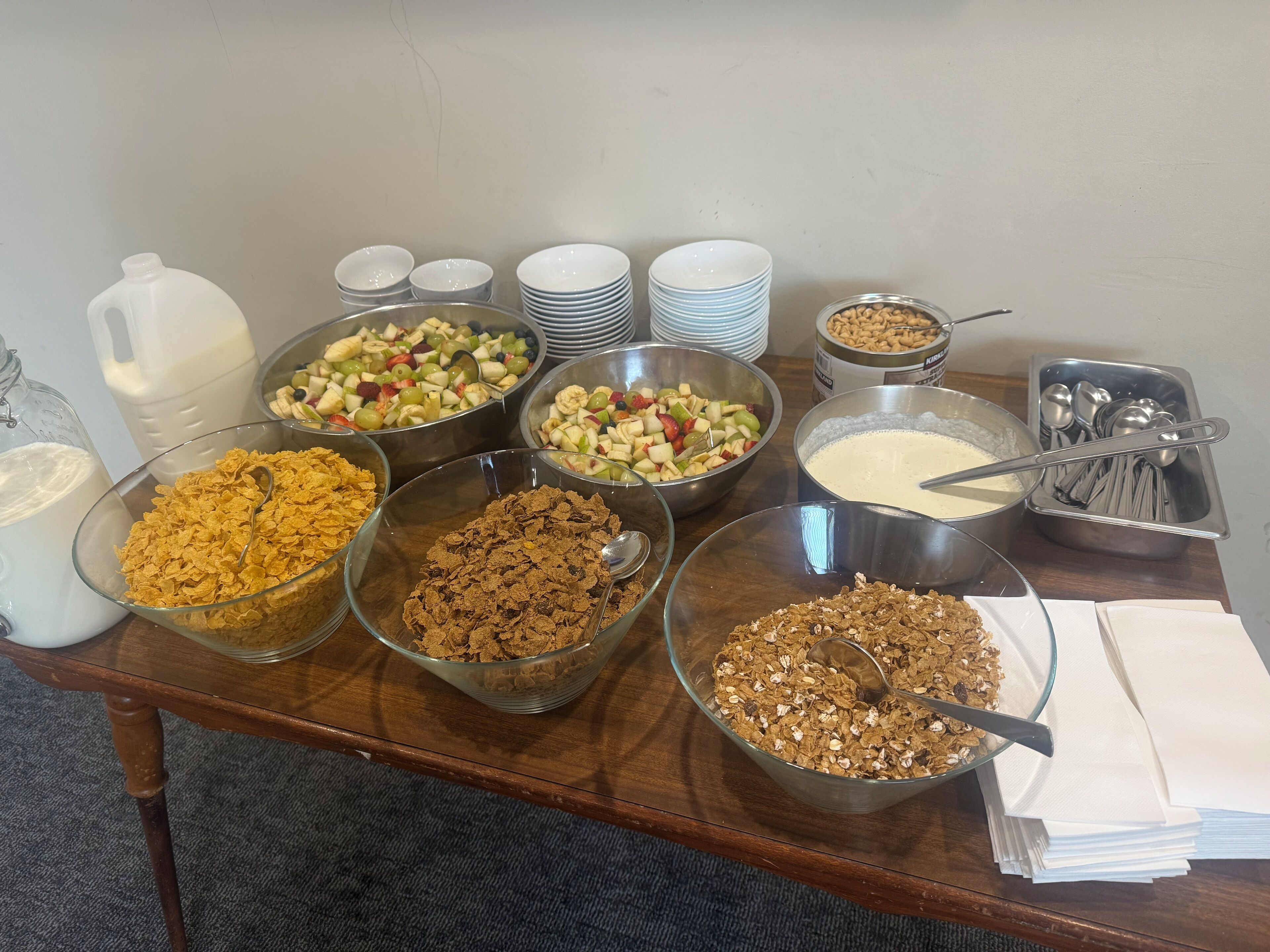 Una mesa de buffet con diversos alimentos, incluyendo cereales, frutas y una jarra de leche.