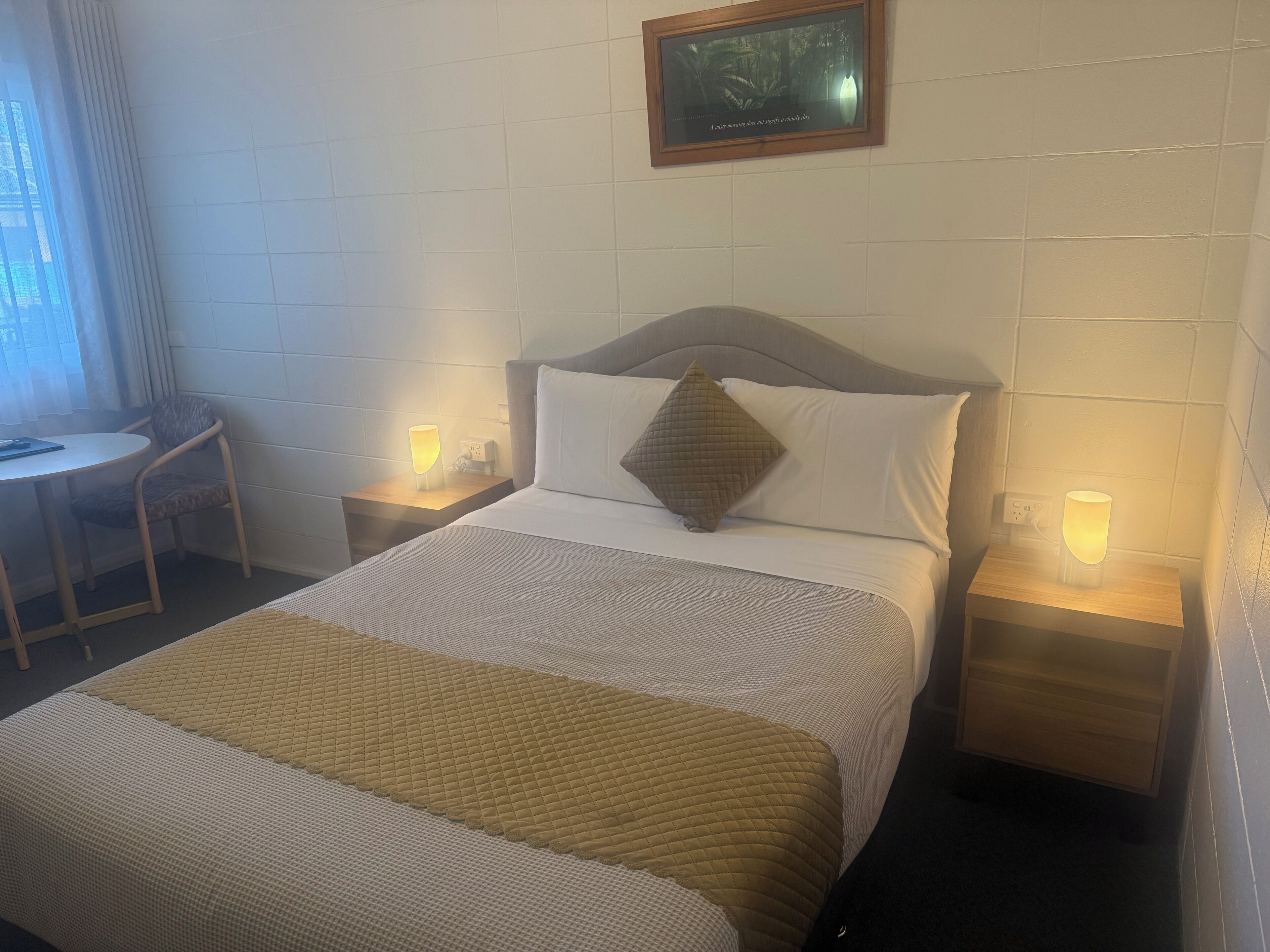 A neatly arranged hotel room with a bed, bedside tables, a chair, and a small table.