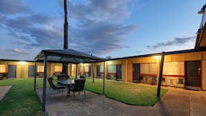 A hotel with a covered outdoor seating area, multiple rooms with doors, and a well-maintained lawn. - Cootamundra Gardens Motel (Cootamundra)