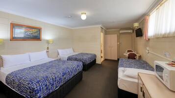 A hotel room with two single beds, a small table with a chair, a microwave, and an air conditioning unit.
