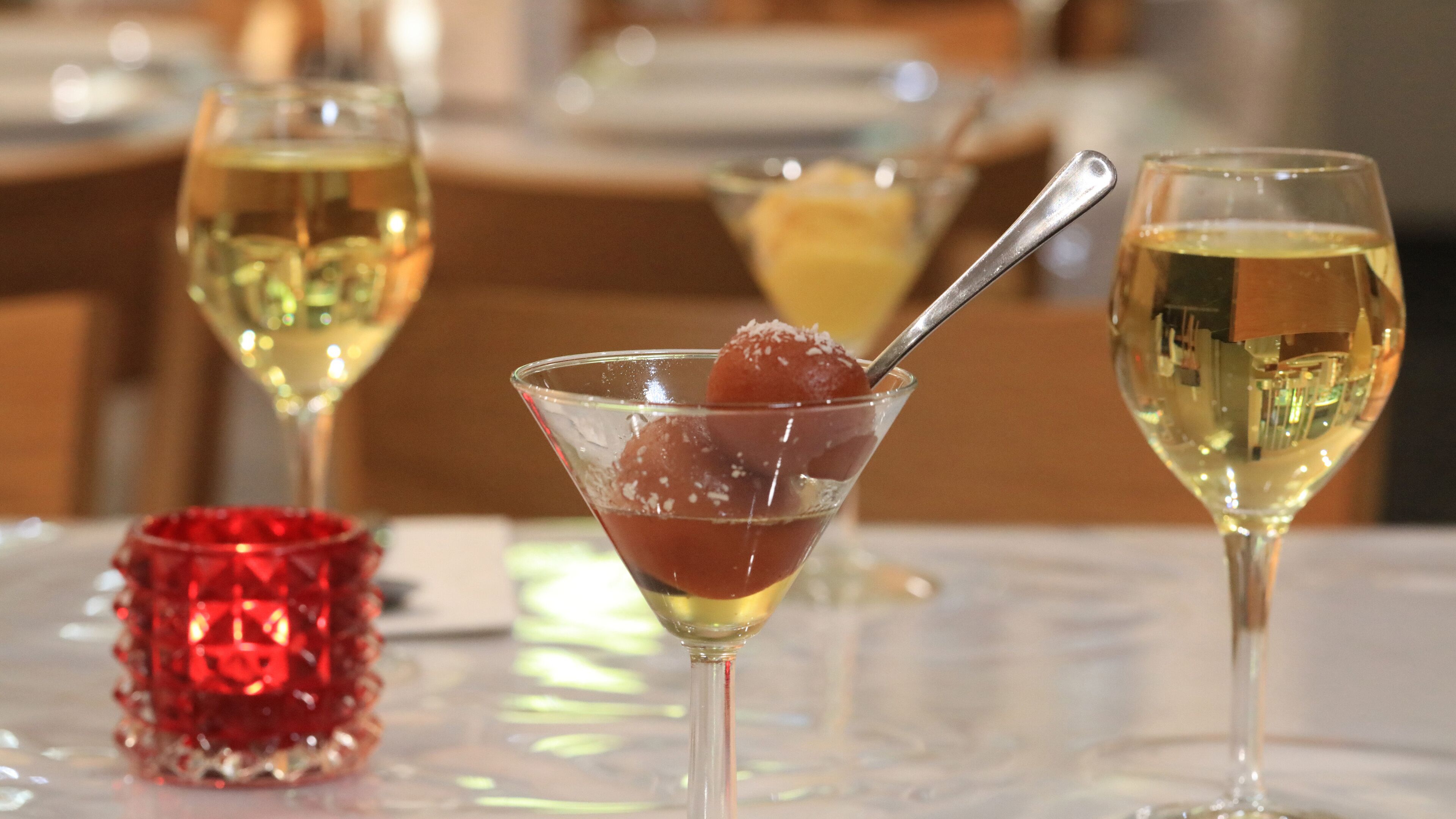 Taula amb tres copes de vi blanc i una copa de martini amb un postre vermell.