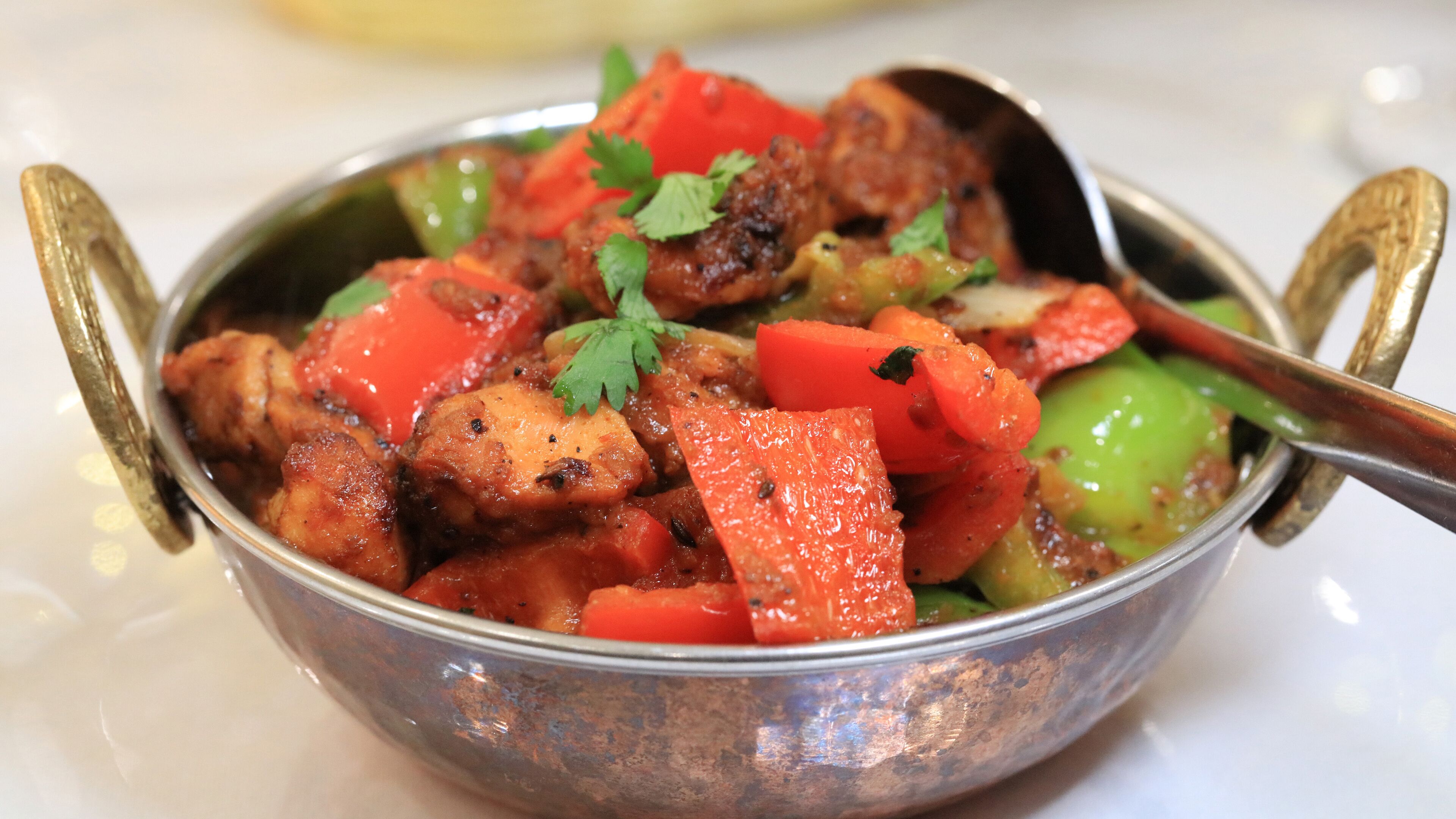 A metal bowl with a spoon, containing a dish with chunks of meat and vegetables.