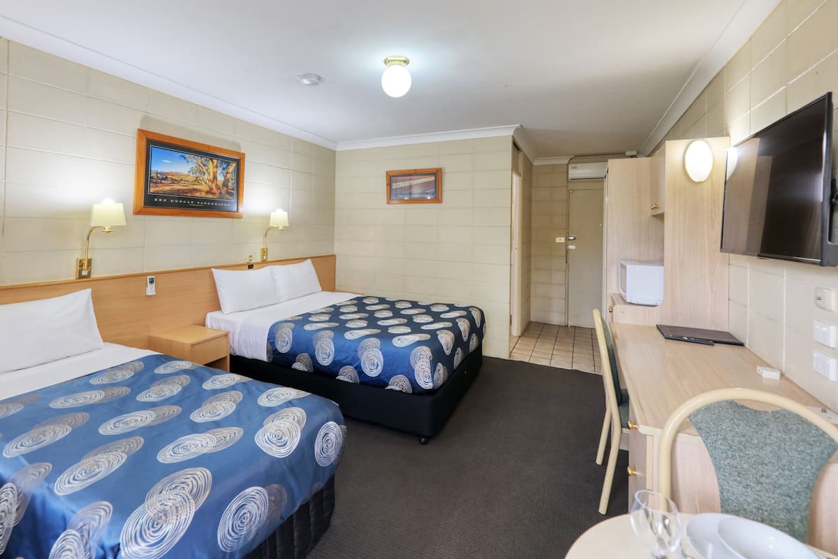 Une chambre d’hôtel avec deux lits, un bureau, une chaise, une télévision et une porte de salle de bain.