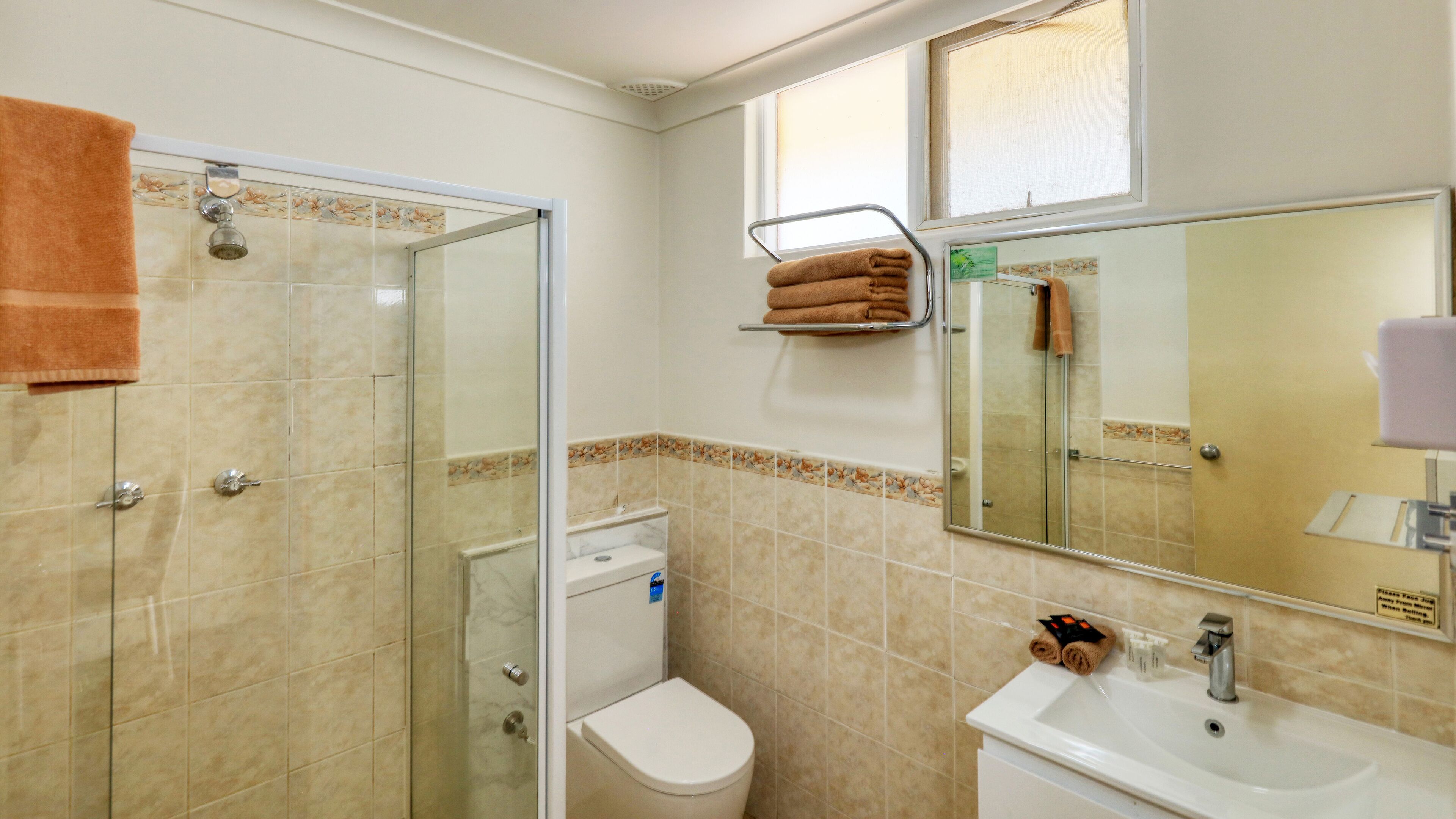 Baño con cabina de ducha de vidrio, inodoro, lavamanos y espejo.