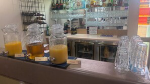 A bar area with a variety of liquor bottles, a selection of glasses, and a juice dispenser with orange and apple juices. - Cootamundra Gardens Motel (Cootamundra)