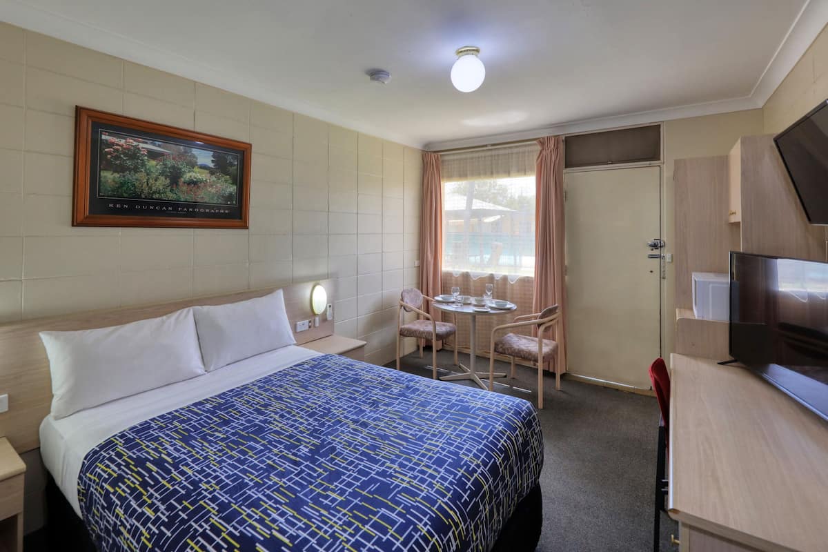 Une chambre d’hôtel comprenant un lit, des tables de chevet, un bureau avec une télévision, une chaise, une petite table avec des verres et une fenêtre avec des rideaux.