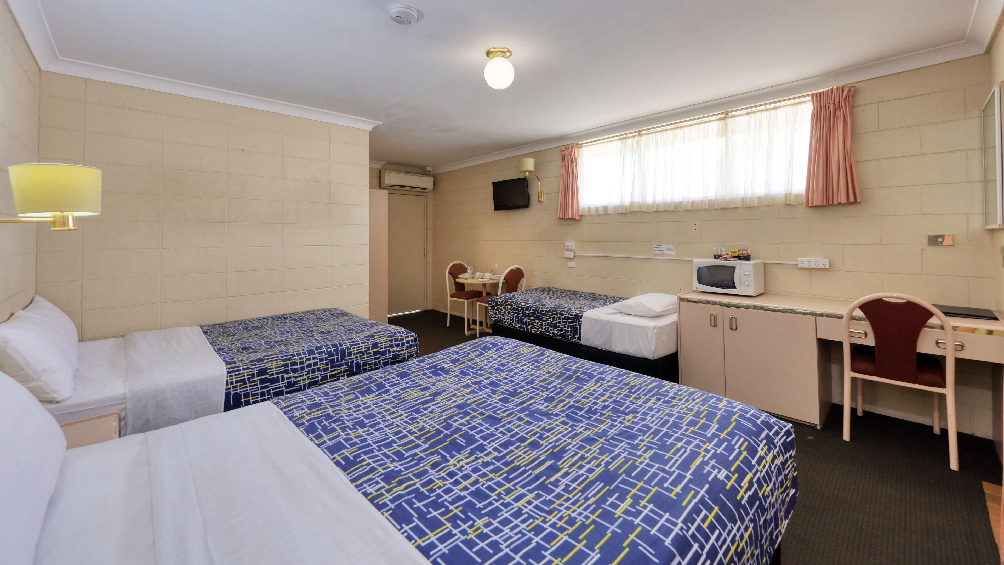 A hotel room with two beds, a desk, a chair, a television, and a window with curtains.