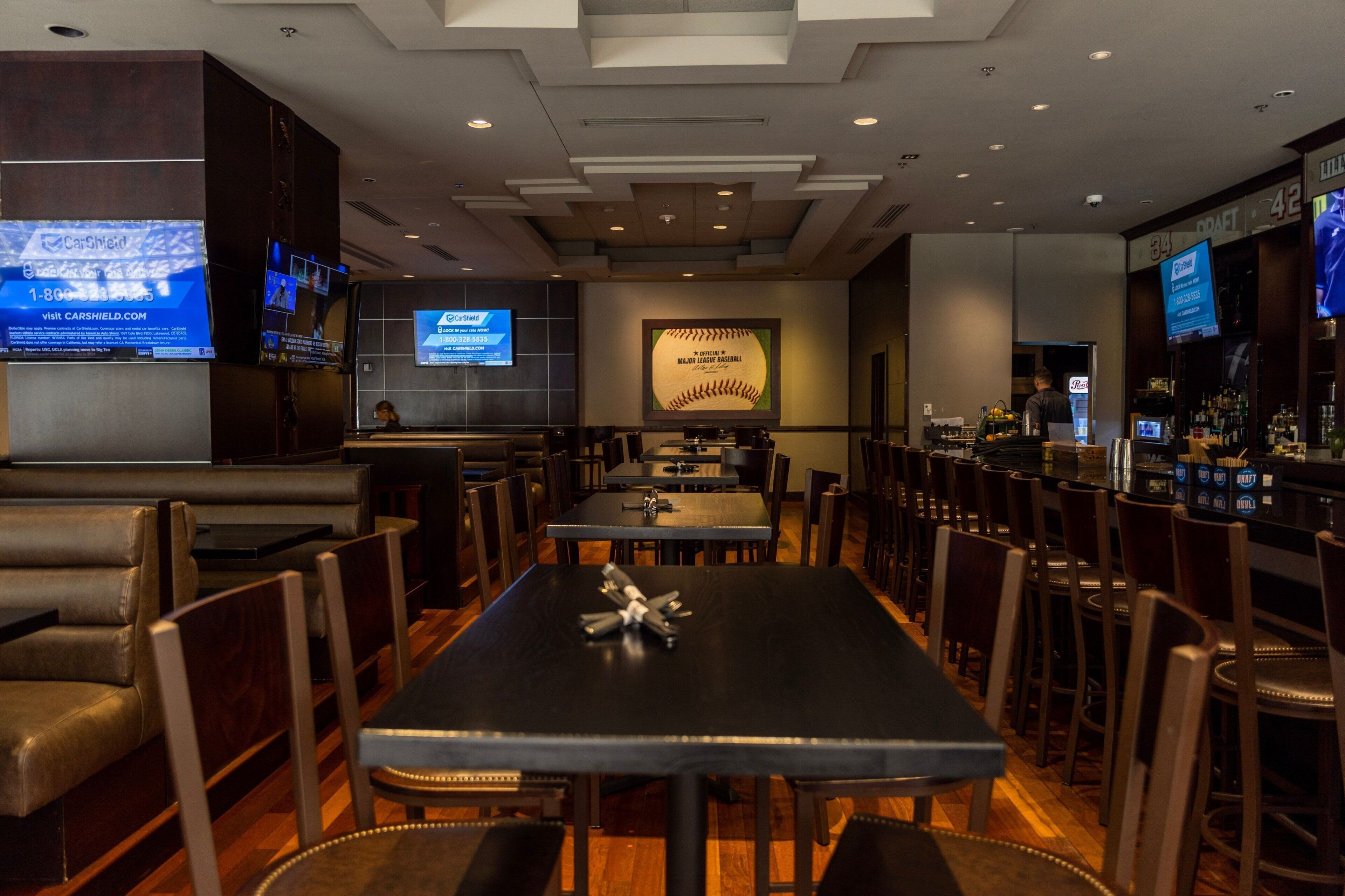 A restaurant with booths and tables, a bar area, and a large screen displaying content.