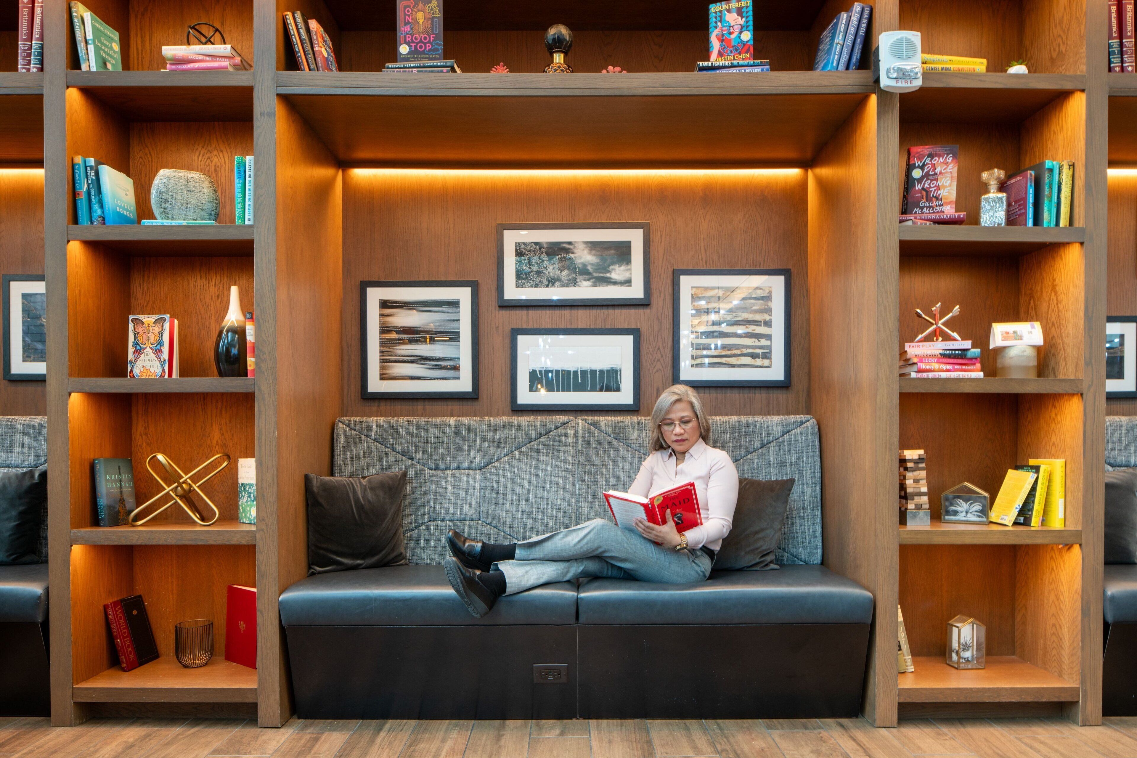 A person sitting on a sofa in a room with wooden shelves containing books and framed pictures.