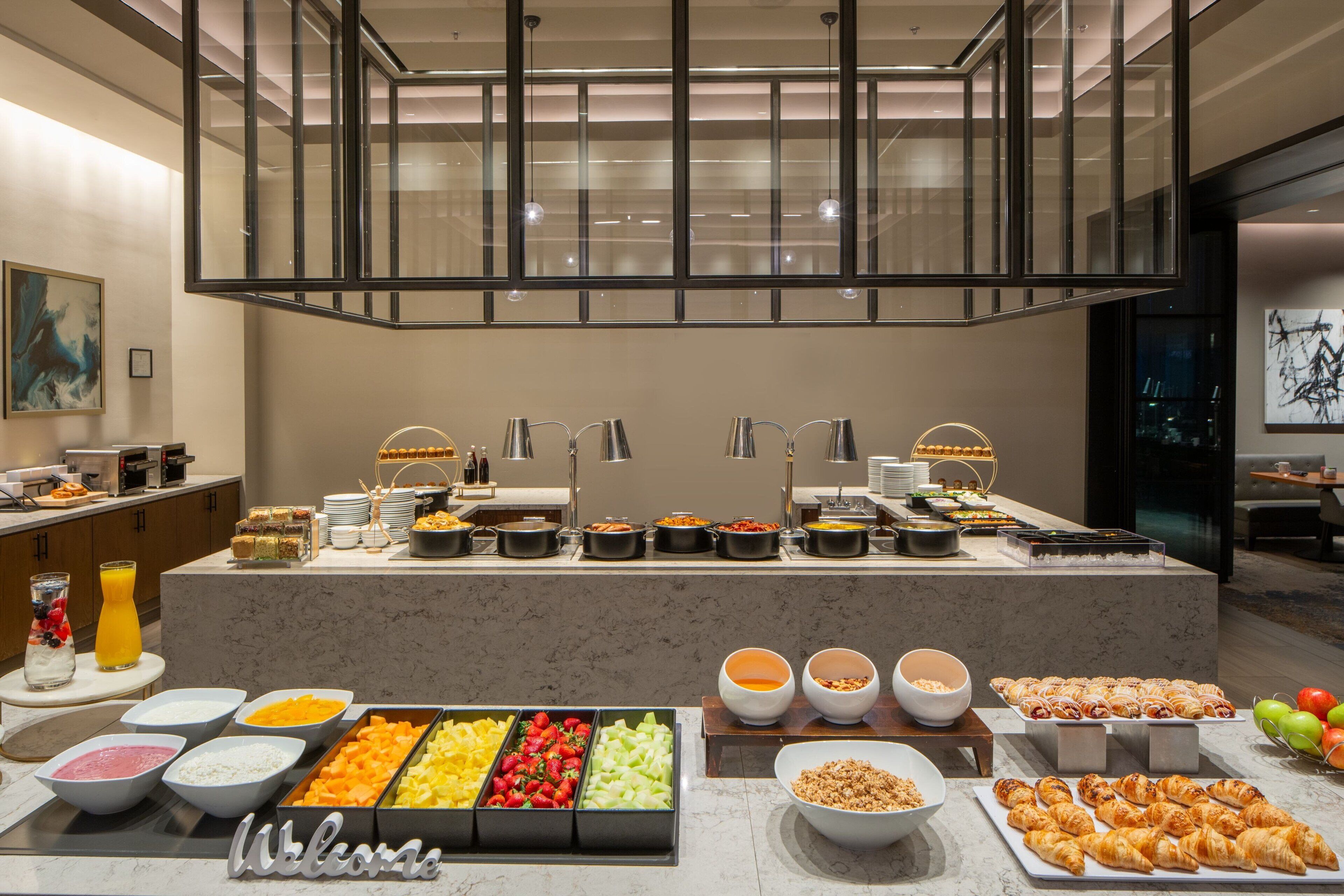 A buffet with various food items and beverages, a glass railing, and a modern interior design.