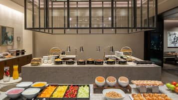 A buffet with various food items and beverages, a glass railing, and a modern interior design.