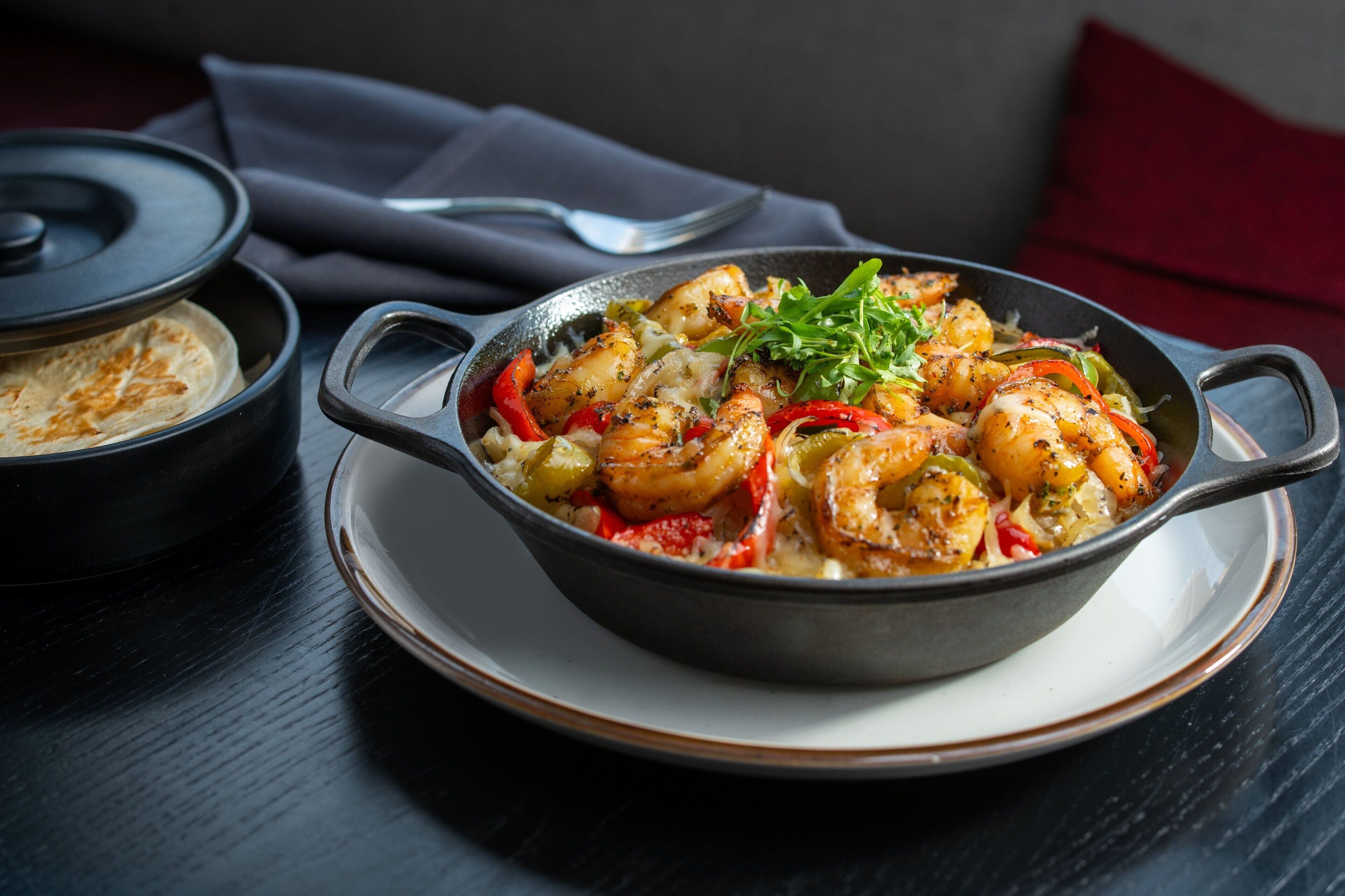 A dish of grilled shrimp with vegetables in a skillet on a plate.