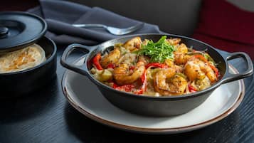 A dish of grilled shrimp with vegetables in a skillet on a plate.