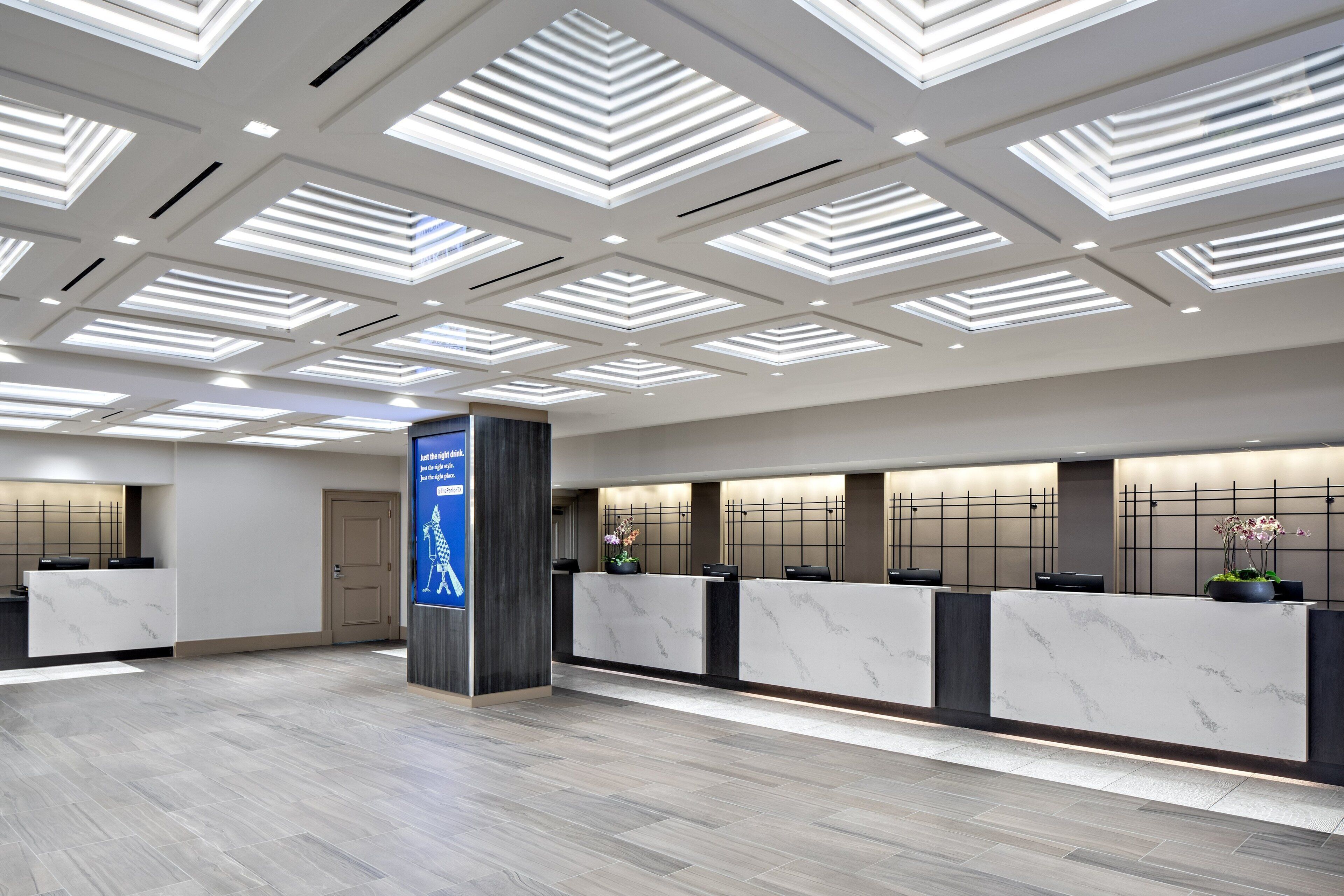 Et moderne receptionsområde med en skrivebord i marmor, et blåt skilt med pile og et loft med lange lysarmaturer.