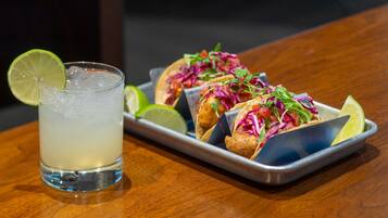 Una bandeja de tacos con una cuña de lima y un vaso de una bebida transparente sobre una mesa de madera.