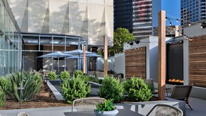 An outdoor patio with seating, a fire feature, and a view of a modern building. - Sheraton Dallas Hotel (Dallas)