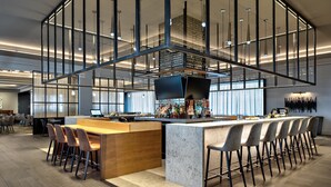 A modern bar area with a long counter, bar stools, and a television screen. - Sheraton Dallas Hotel (Dallas)
