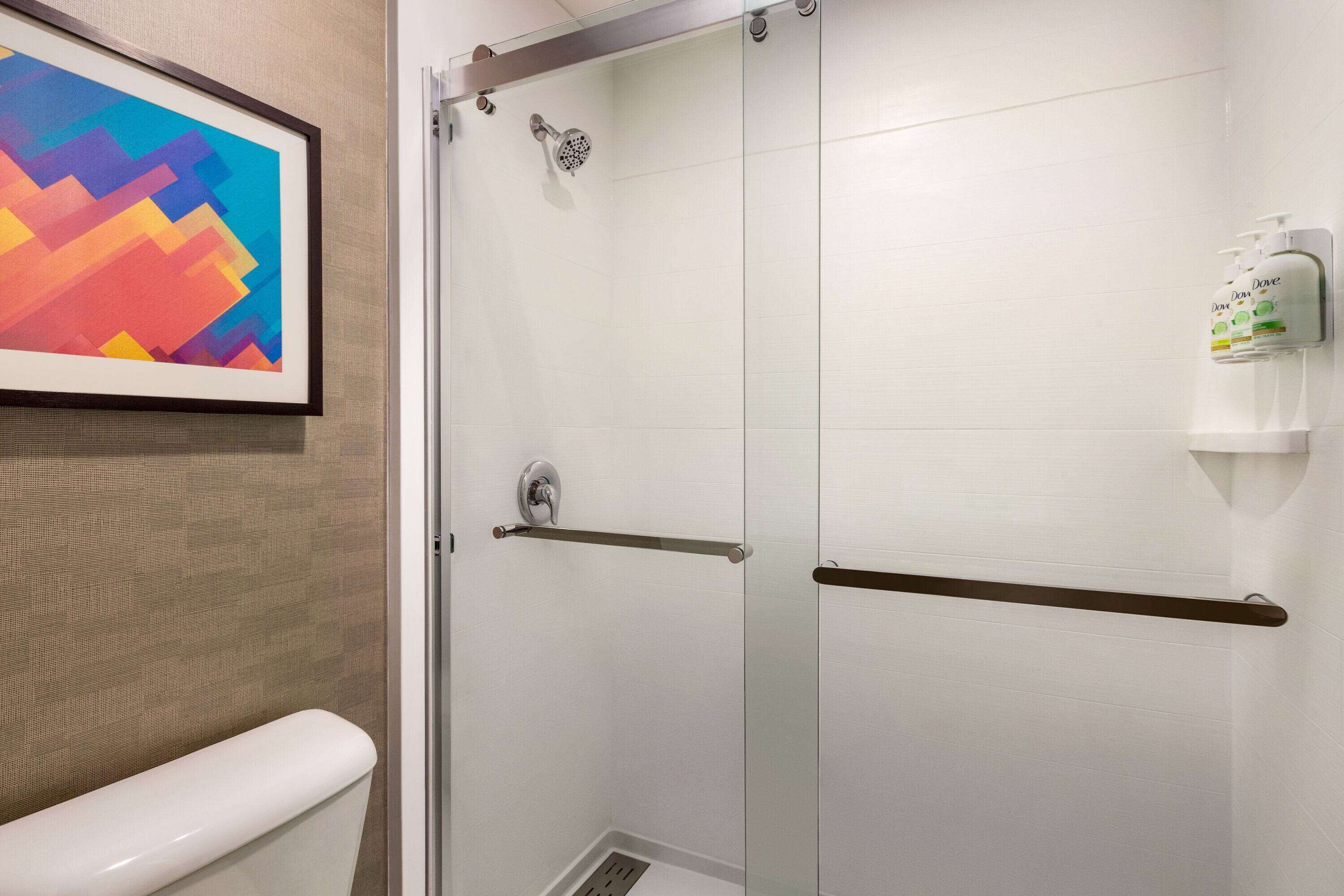 A bathroom with a glass shower enclosure, a towel rack, and a framed artwork on the wall.