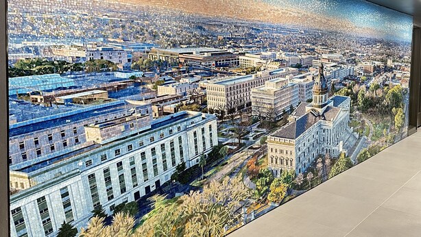 Une mosaïque murale panoramique représentant un paysage urbain avec des bâtiments et de la végétation.