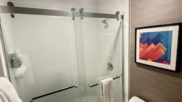 A modern bathroom with a glass-enclosed shower, a white toilet, and a framed abstract painting on the wall.