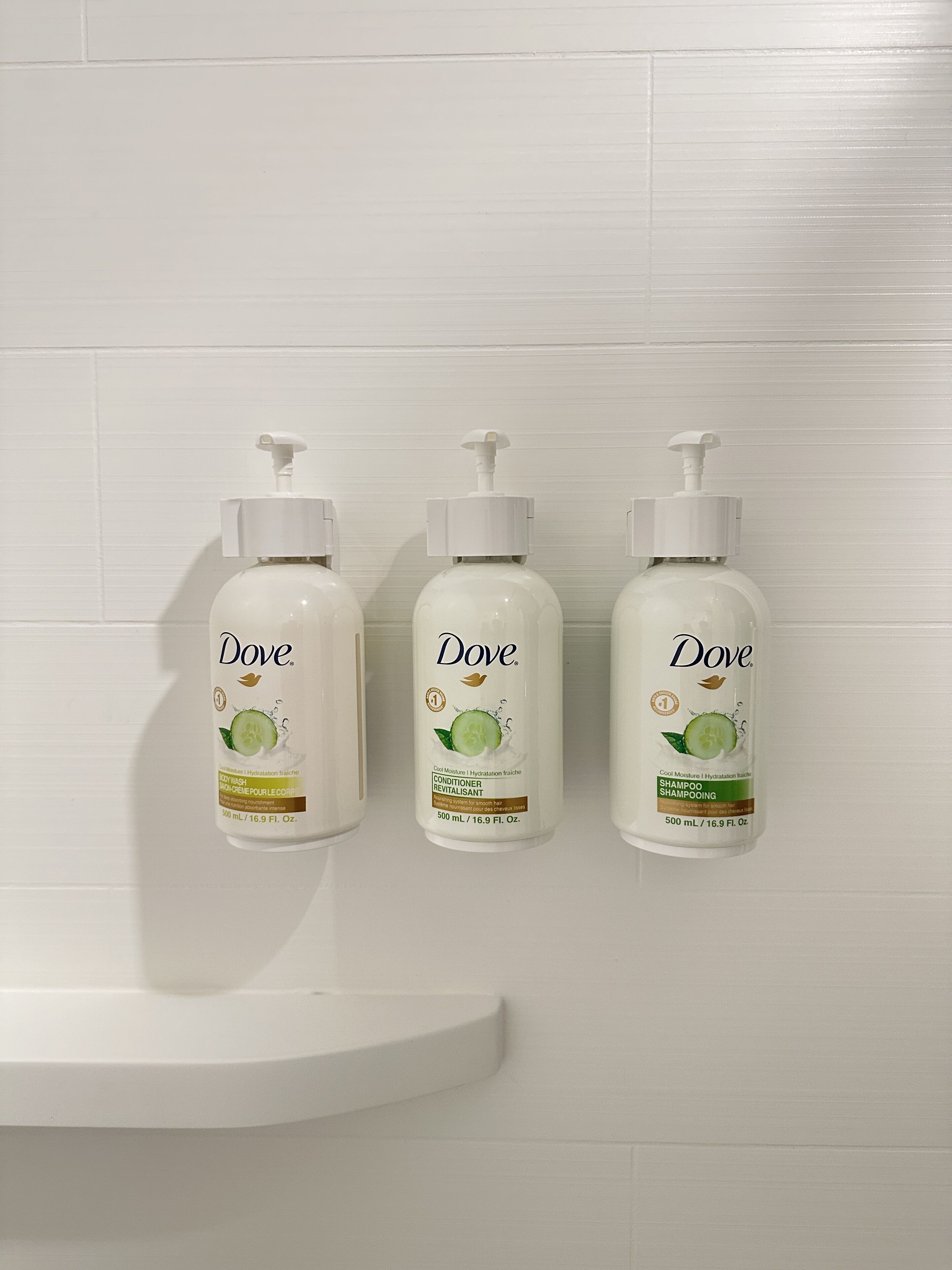 Tre Dove shampoo flasker monteret på en hvid flisevæg.