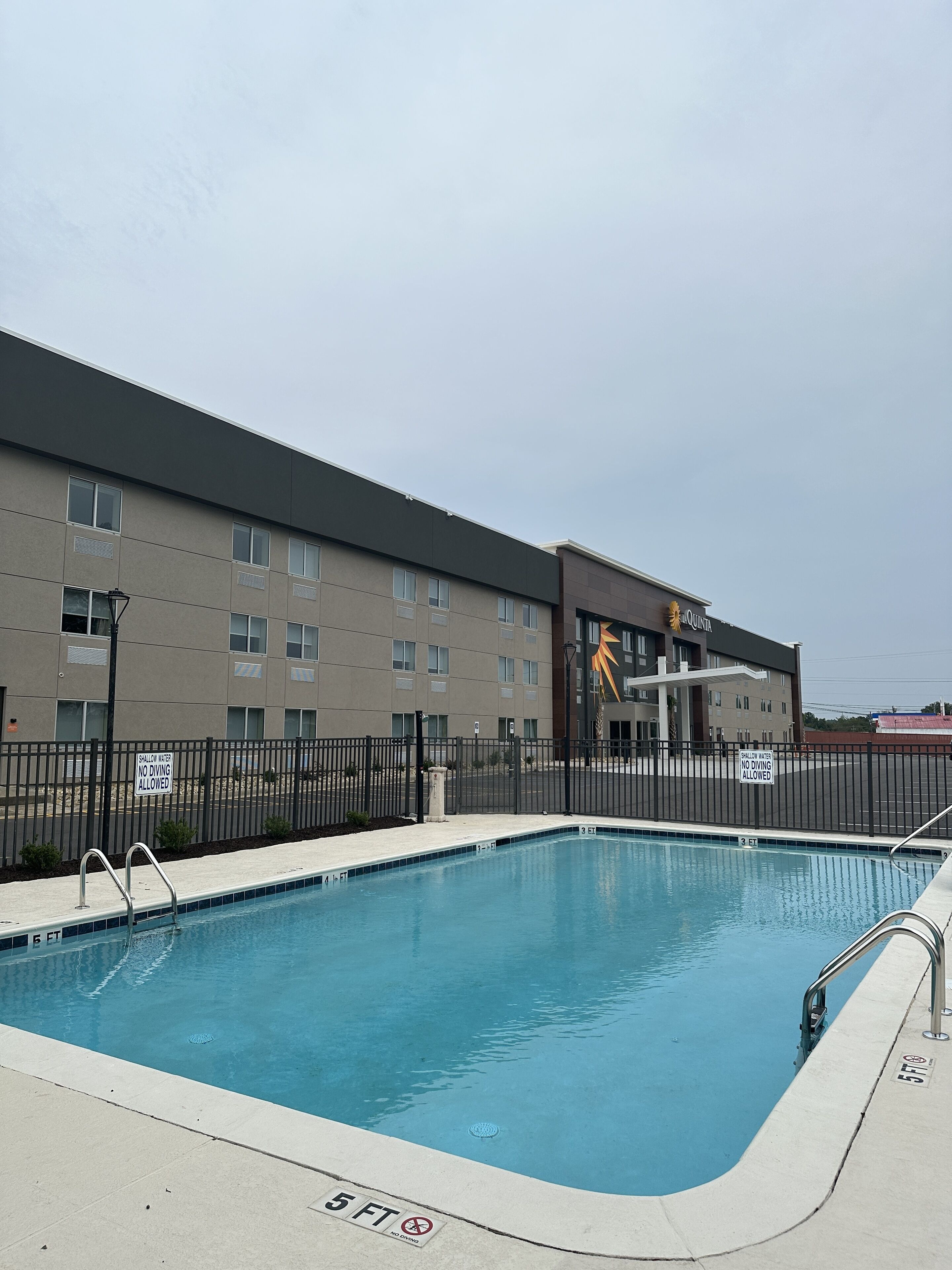 A swimming pool with a no diving sign, a fence, and a building with a sign that reads "QUINTA".