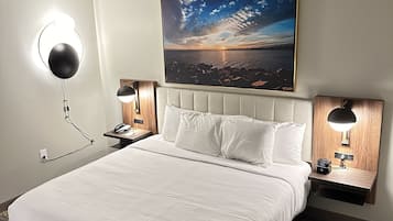 Habitación de hotel con una cama grande, dos mesitas de noche con lámparas, un cuadro colgado en la pared y una alfombra estampada.
