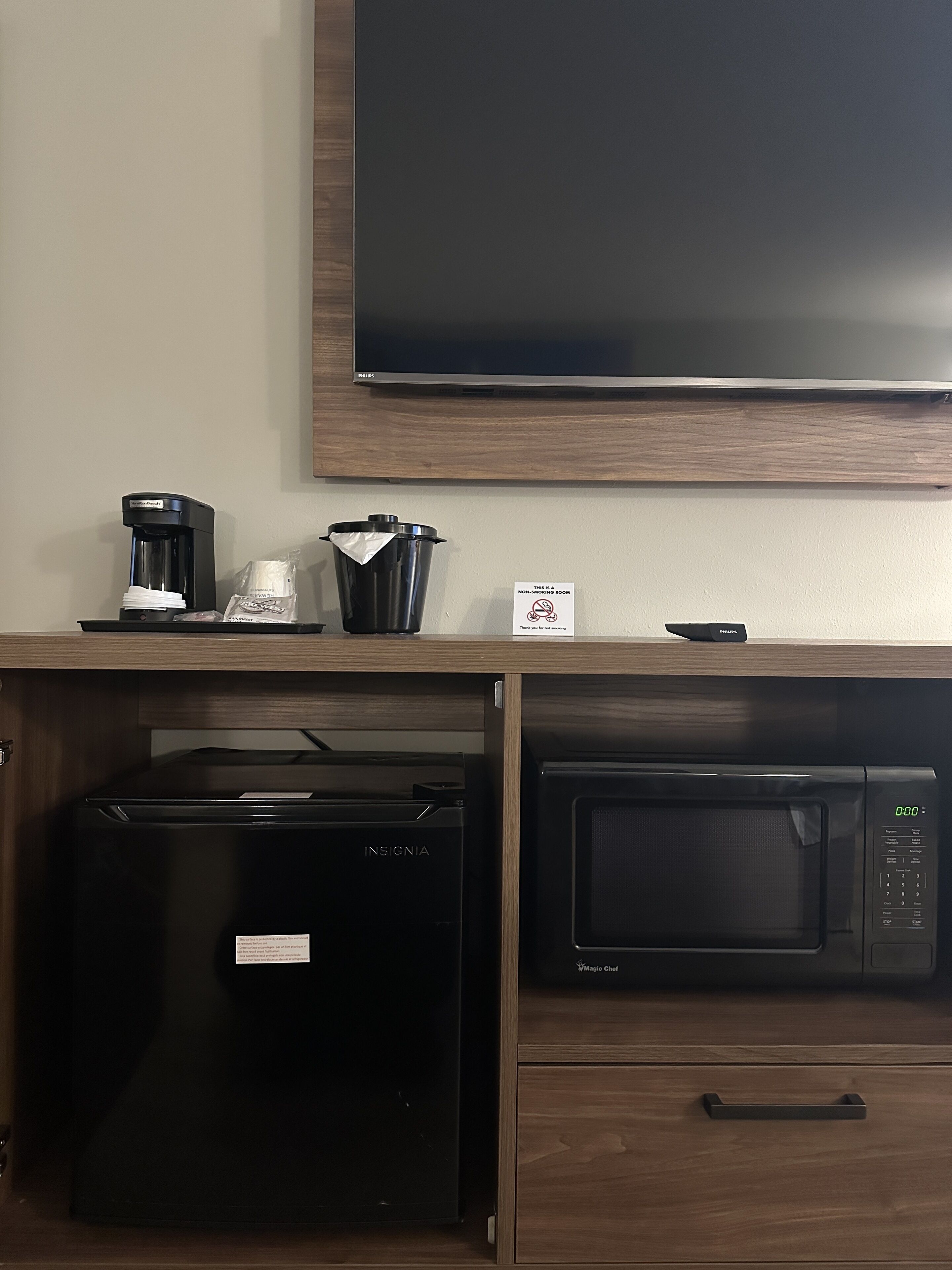 Een kitchenette met een koffiezetapparaat, prullenbak, magnetron en koelkast.