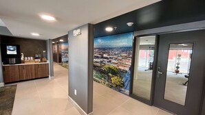 Un hall d’hôtel comprenant un comptoir d’accueil, une grande fresque représentant un paysage urbain et une porte donnant accès à un parking.