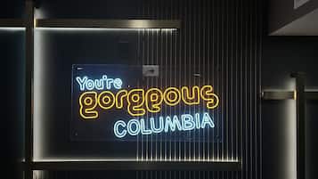 Un letrero de neón con el texto 'You're gorgeous Columbia' sobre un fondo oscuro con líneas verticales.