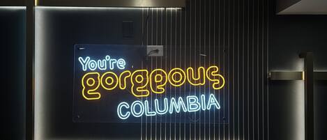 A neon sign with the text "You're gorgeous Columbia" against a dark background with vertical lines.