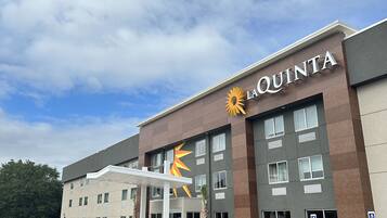 Um hotel chamado La Quinta com design moderno, apresentando um sol proeminente no logotipo, várias janelas e uma área de entrada coberta.