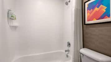 A bathroom with a white bathtub, a showerhead, and a toilet. There is a framed abstract painting on the wall.