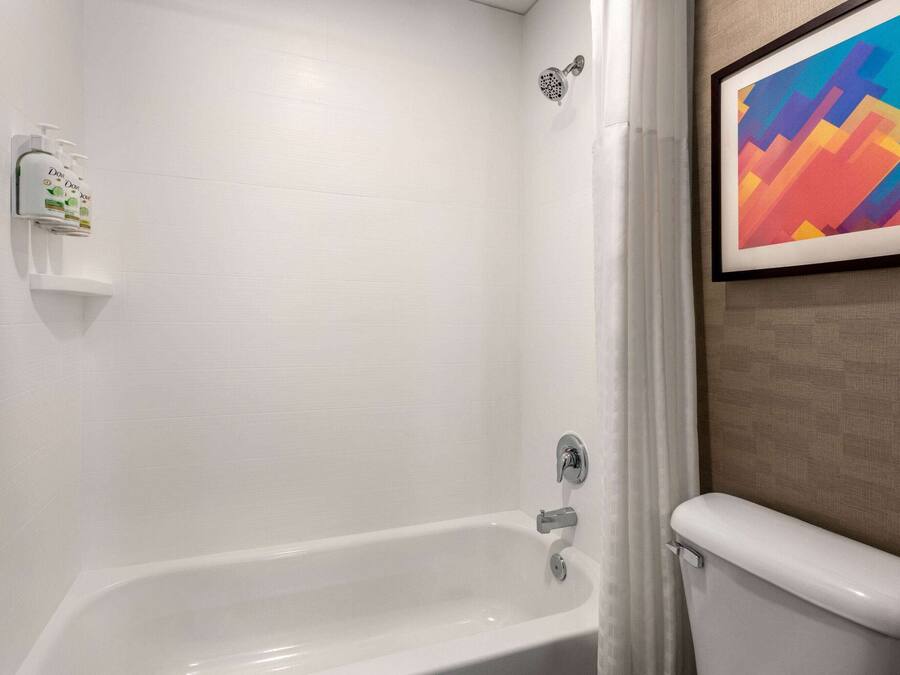 A bathroom with a white bathtub, a showerhead, and a toilet. There is a framed abstract painting on the wall.