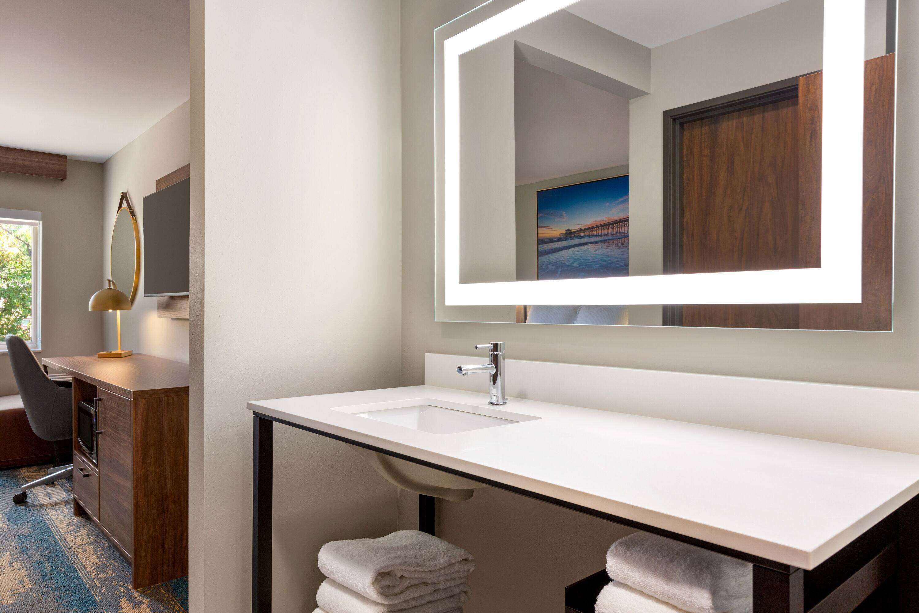 A modern bathroom with a large mirror, a white sink, and a wooden vanity.