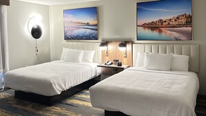 Une chambre d’hôtel avec deux lits, une table de chevet avec un téléphone et une lampe, et deux grandes peintures représentant des paysages accrochées au mur.