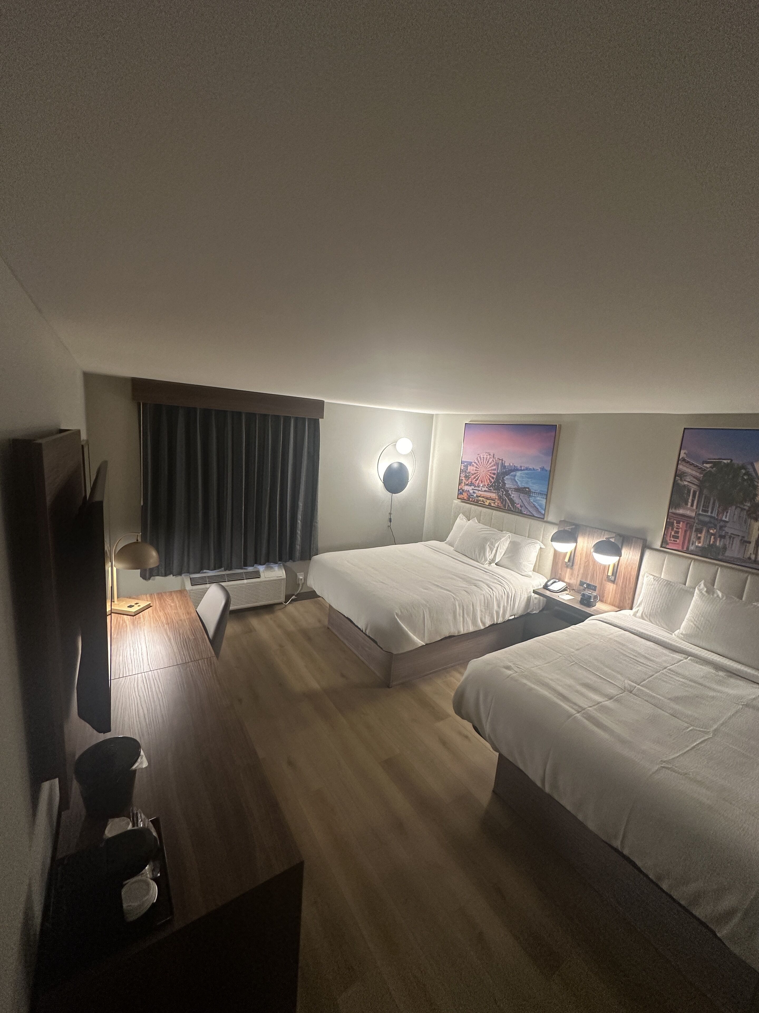 A hotel room with two beds, a desk, a chair, a lamp, and a painting on the wall.