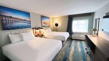 Habitación de hotel con dos camas, un escritorio, una silla, un ventanal grande y obras de arte en las paredes.
