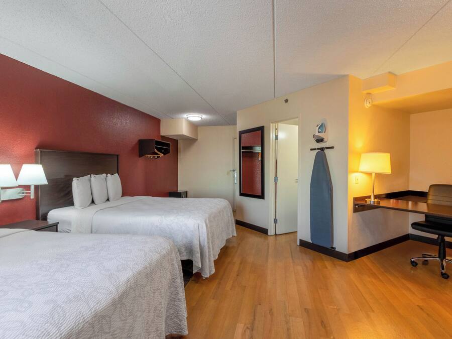A hotel room with two beds, a desk, a chair, and a bathroom.