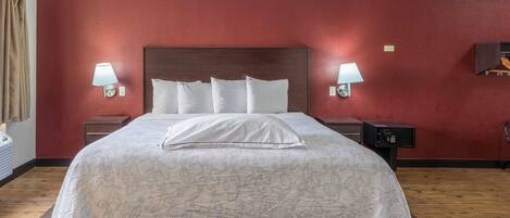A hotel room with a large bed, two bedside lamps, a wooden headboard, and a red wall.